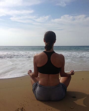 Areti meditating on a beach facing the sea