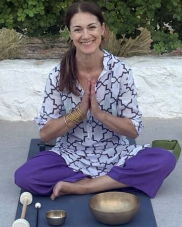 Areti sitting on a yoga mat with Tibetan singing bowls in front of her